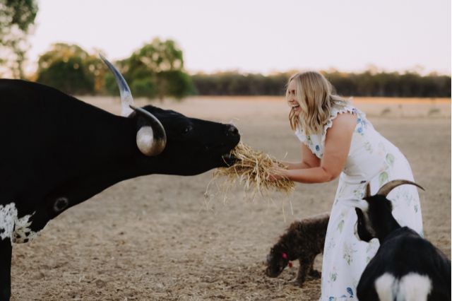 Cassie laughing while feeding hay to her farm animals, showcasing her relaxed and warm nature as a Central Victoria celebrant.